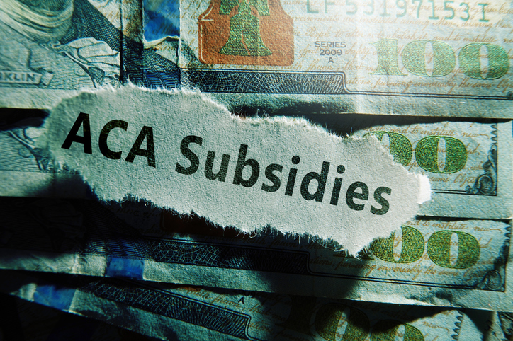 ACA Subsidies newspaper headline on hundred dollar bills -- Affordable Care Act aka Obamacare healthcare premium subsidy concept