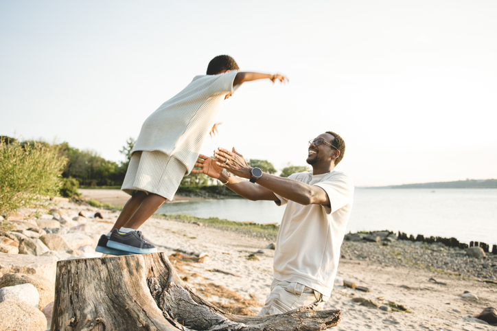 Cheerful black american father and is son against beautiful seascape