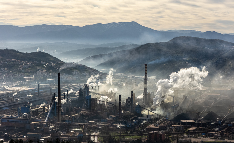 Aerial view of a large industrial factory complex with smokestacks releasing smoke into the air