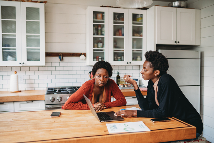 Women managing home finances, discussing budget on laptop