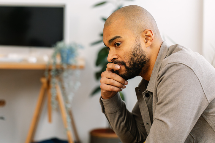 Young adult man worried sitting on sofa at home