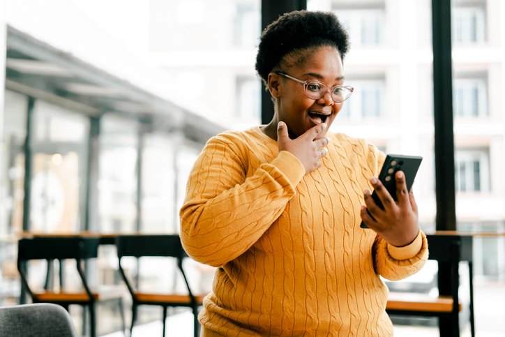 Young black woman receiving surprising news on smartphone