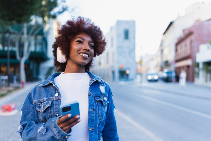 Woman with afro hairstyle walking on street holding smartphone and smiling