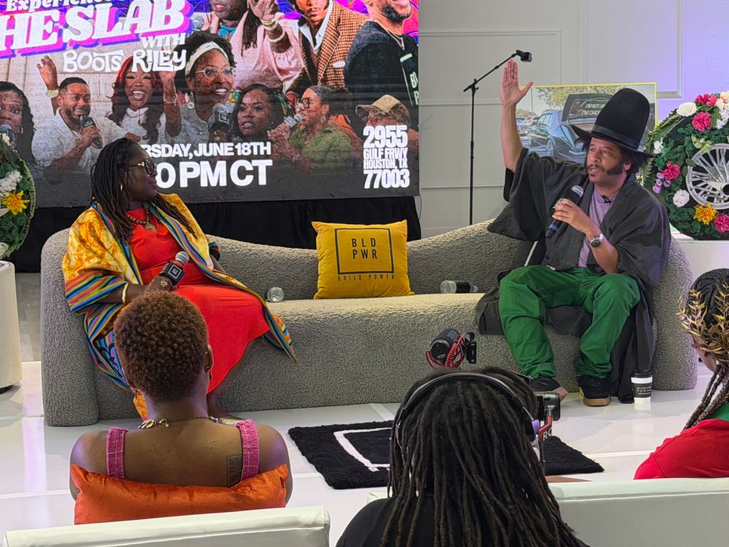 A group of people sitting on a couch, with a large event poster in the background advertising "Experience He Slab" with Boots Riley on June 18th at 10PM CT.