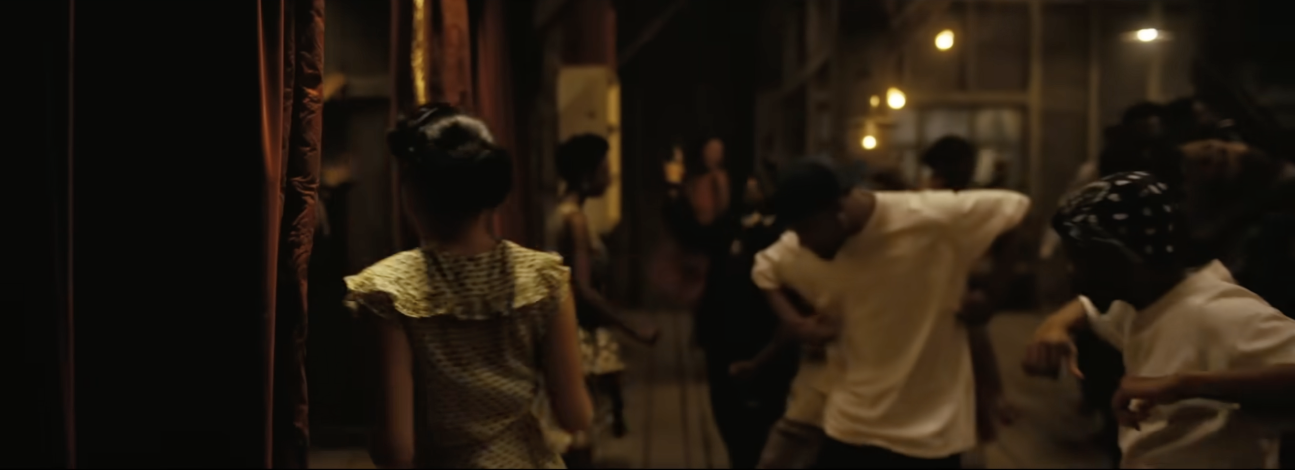 A dimly lit indoor scene with several people gathered, some dancing and others observing.