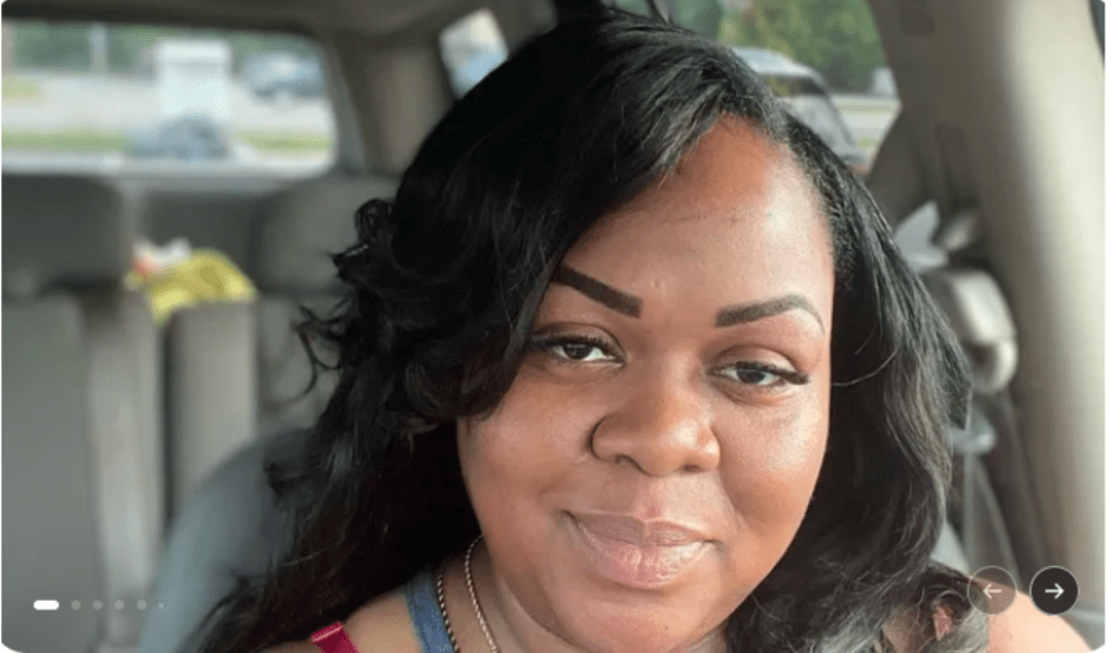 A smiling middle-aged Black woman with long dark hair in a car.