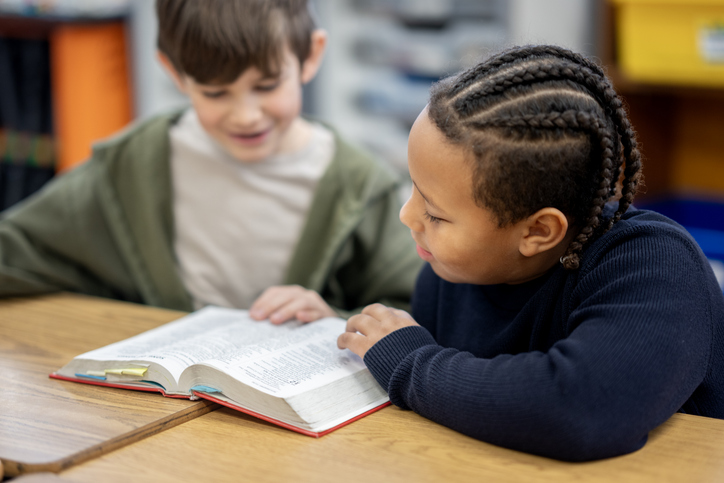 Two Children Reading Together At A Classroom Table During Elementary School Group Reading Activity