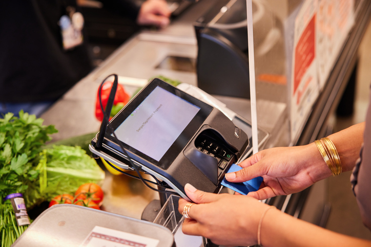 Woman paying for groceries with her credit card at a plexiglass protected checkout