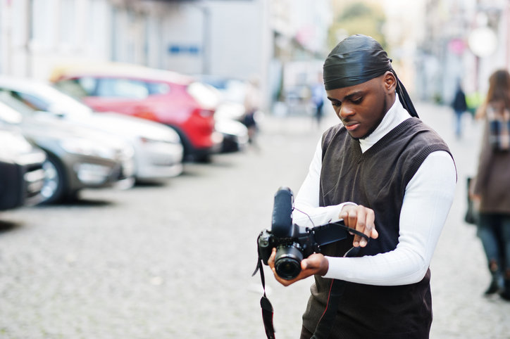 Young professional african american videographer holding professional camera with pro equipment. Afro cameraman wearing black duraq making a videos.