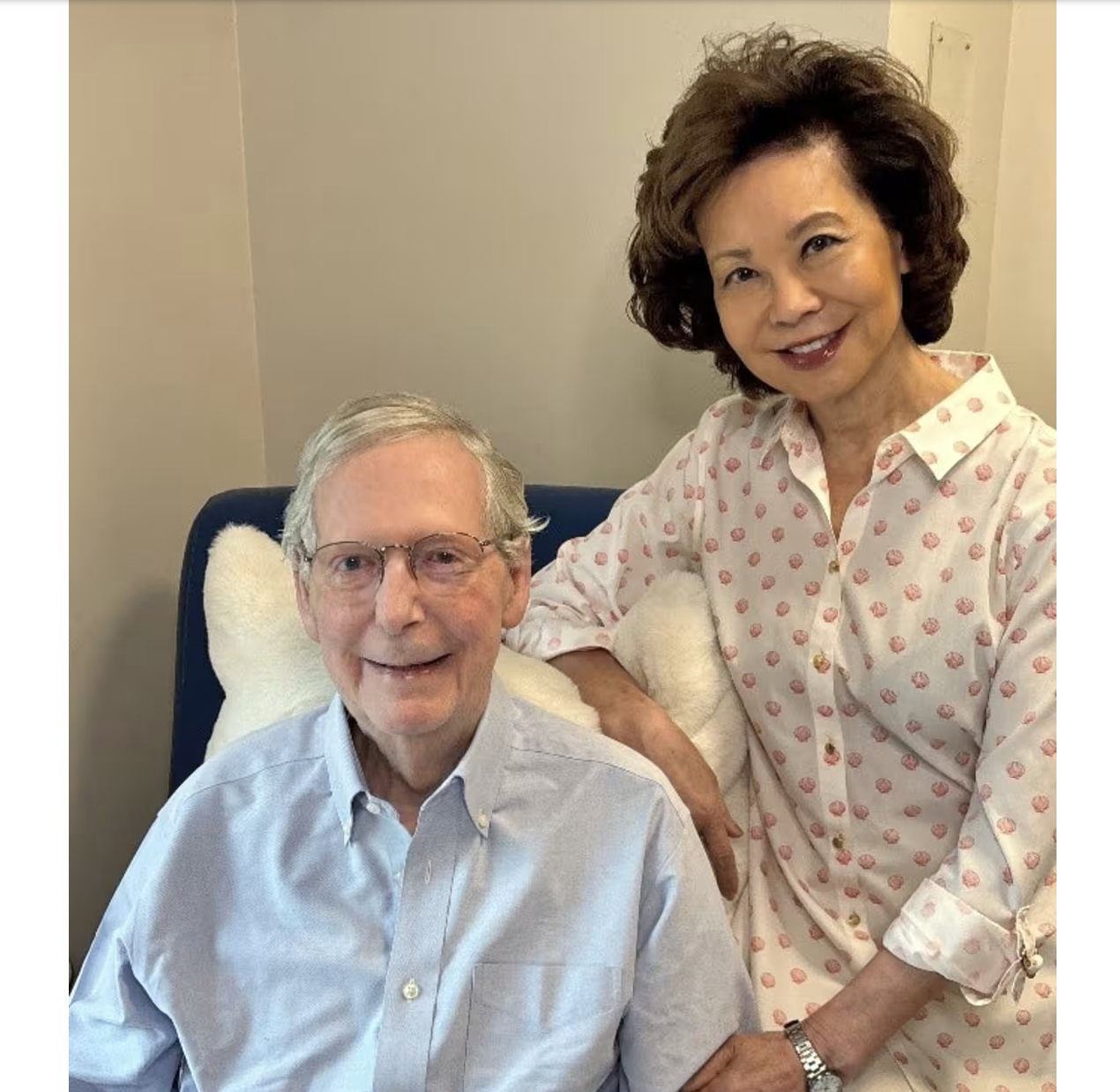An older man with gray hair and glasses smiling while a woman with curly dark hair in a polka dot blouse stands next to him, also smiling.