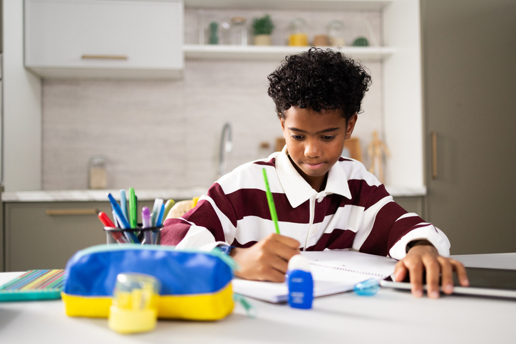 Young boy doing homework at kitchen table, concentrating on schoolwork