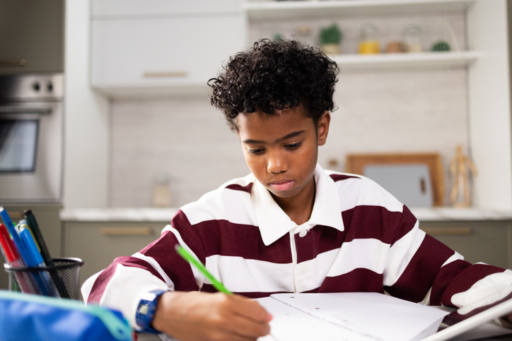 Boy writing homework in notebook for school at home