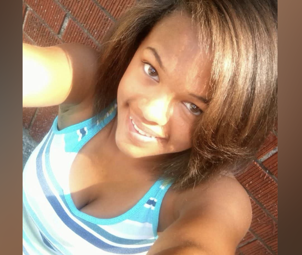 A smiling woman with long brown hair wearing a blue and white striped tank top.