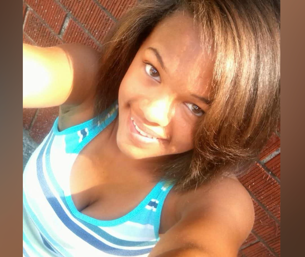 A smiling woman with long brown hair wearing a blue and white striped tank top.
