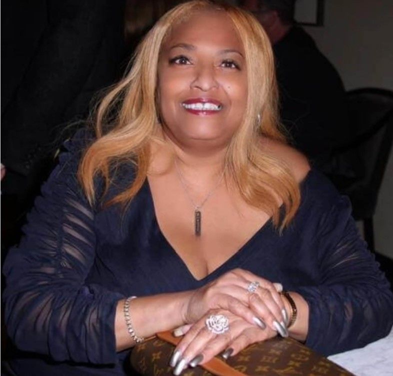 A smiling woman with long blonde hair wearing a black jacket and jewelry.