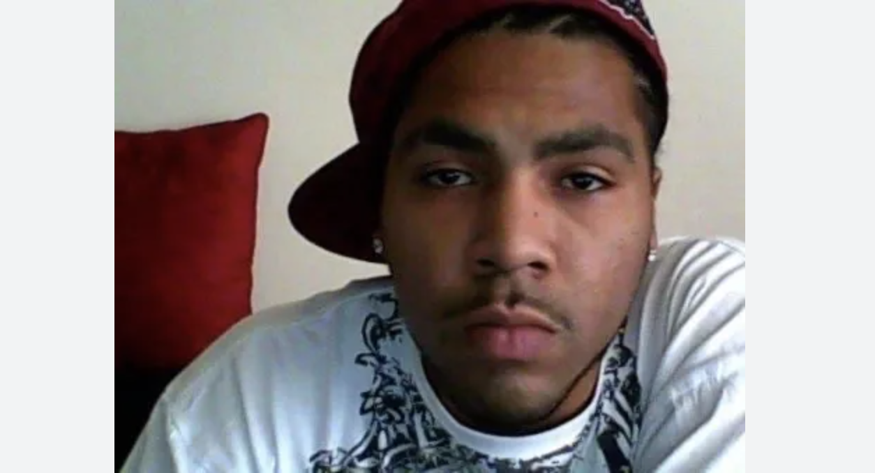 A young man wearing a red hat and a white shirt with a graphic design, looking directly at the camera with a serious expression.