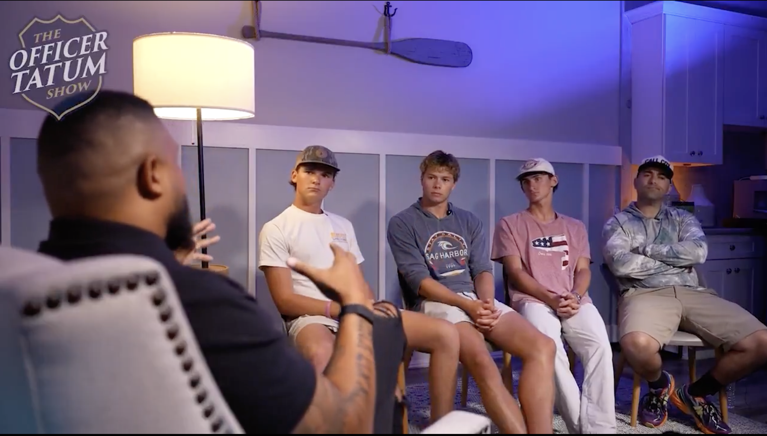 A group of young men sitting in a room with a sign that says "The Officer Tatum Show" visible in the background.