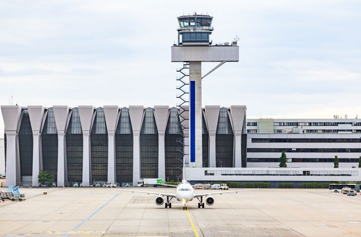Commercial passenger airplane taxiing on tarmac apron with air traffic control tower and terminal building at Frankfurt airport on background