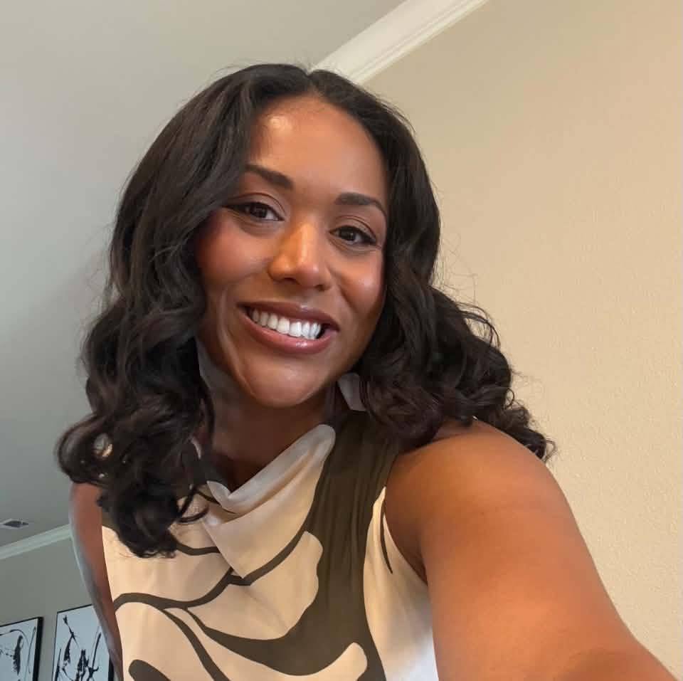 A smiling woman with curly dark hair wearing a beige patterned scarf.