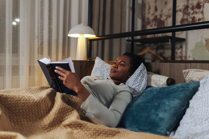 Mid Adult Black Woman Reading a Book in Bed Before Sleep