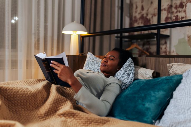 Mid Adult Black Woman Reading a Book in Bed Before Sleep