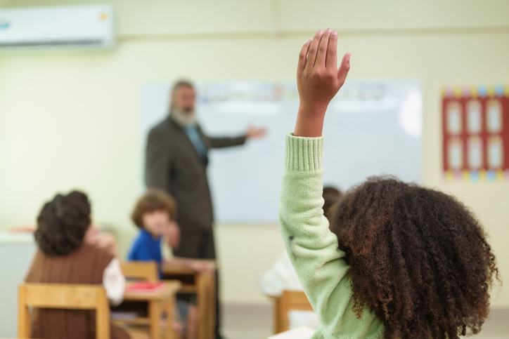 Student raises a hand to answer a classroom question, showing confidence, participation, and active engagement during an interactive school lesson.
