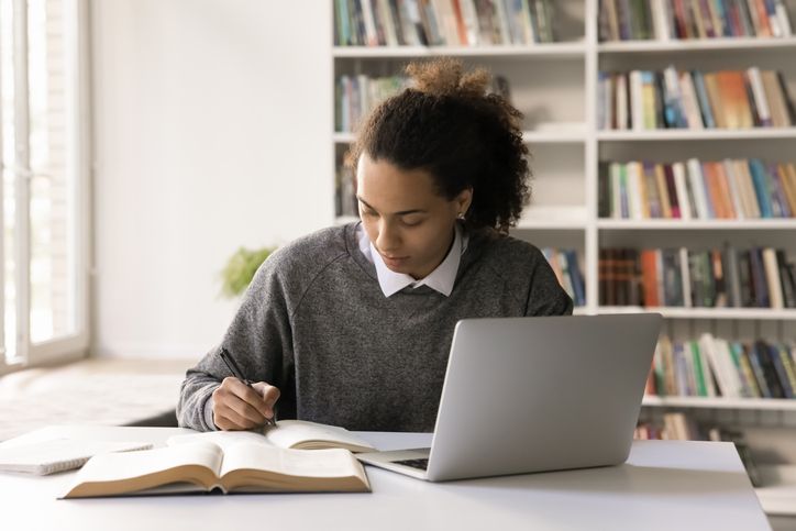 Focused male student work on project at library using notebook