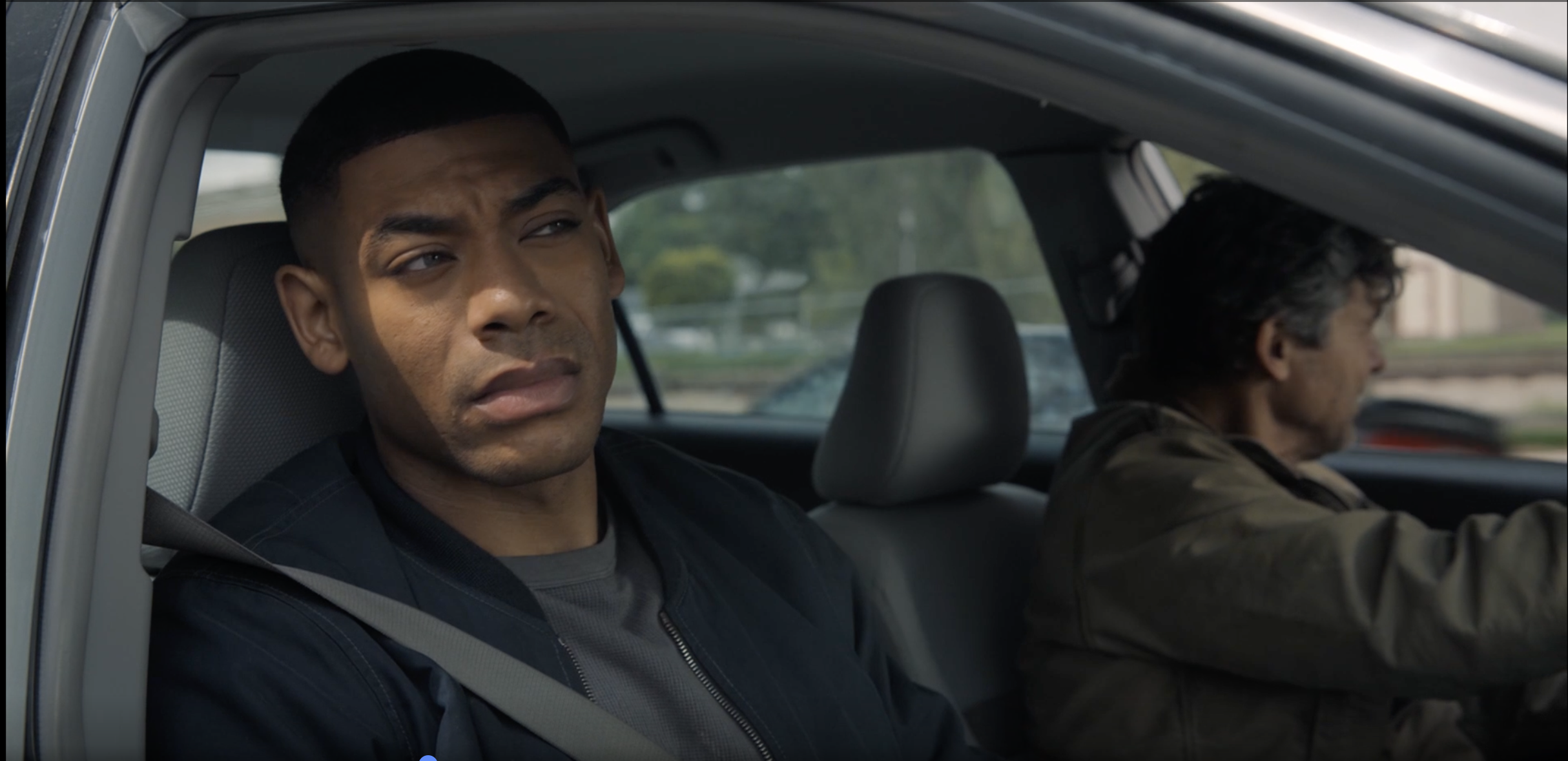 A man sitting in the driver's seat of a car, looking concerned or thoughtful.