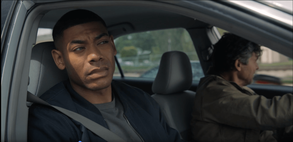 A man sitting in the driver's seat of a car, looking concerned or thoughtful.