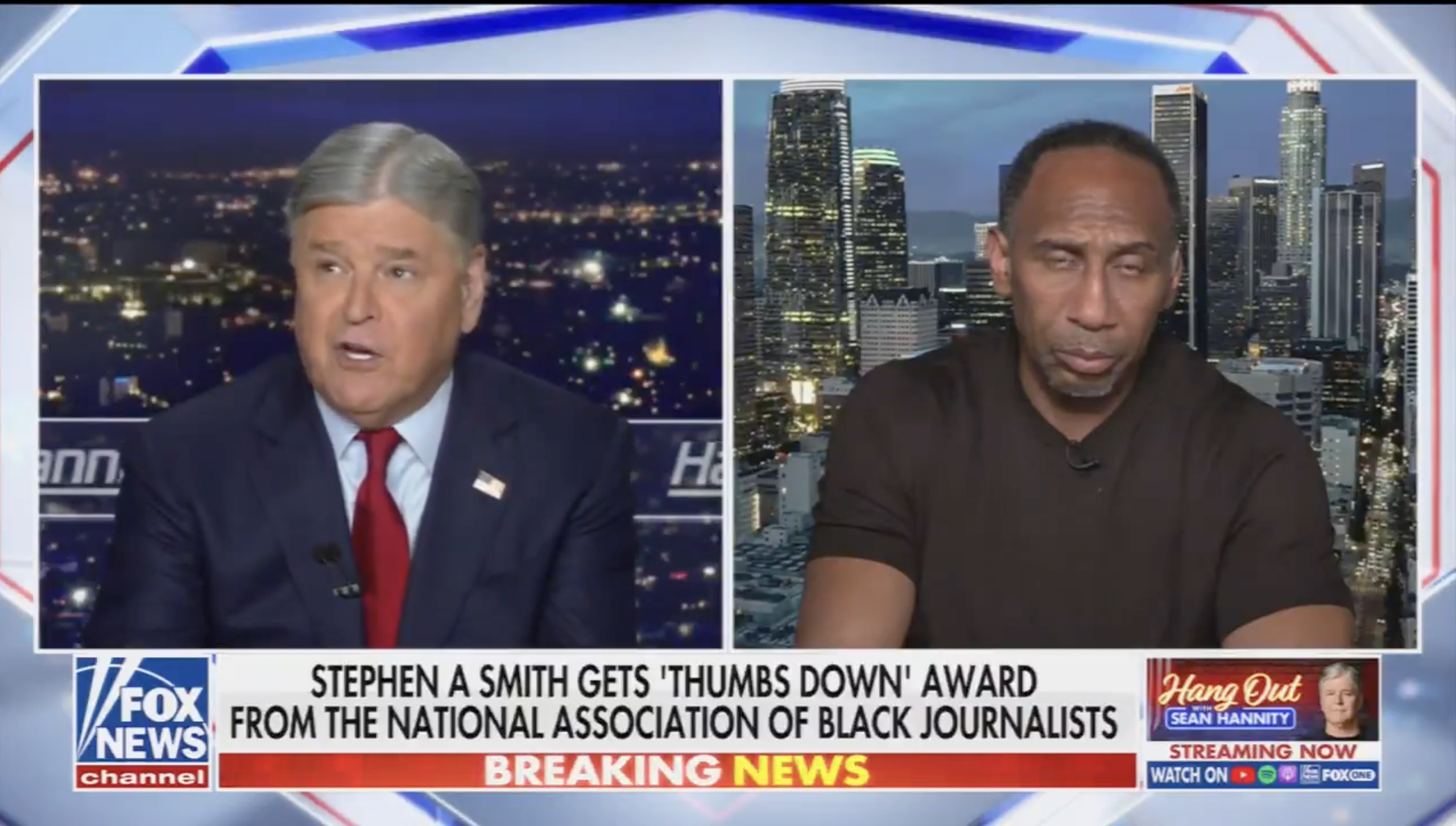 Two news anchors, one on the left wearing a red tie and the other on the right wearing a brown shirt, discussing a news story on the screen behind them showing a city skyline at night.