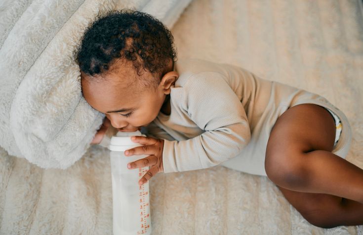 Young Baby Drinking Milk From Bottle On Soft Blanket Indoors