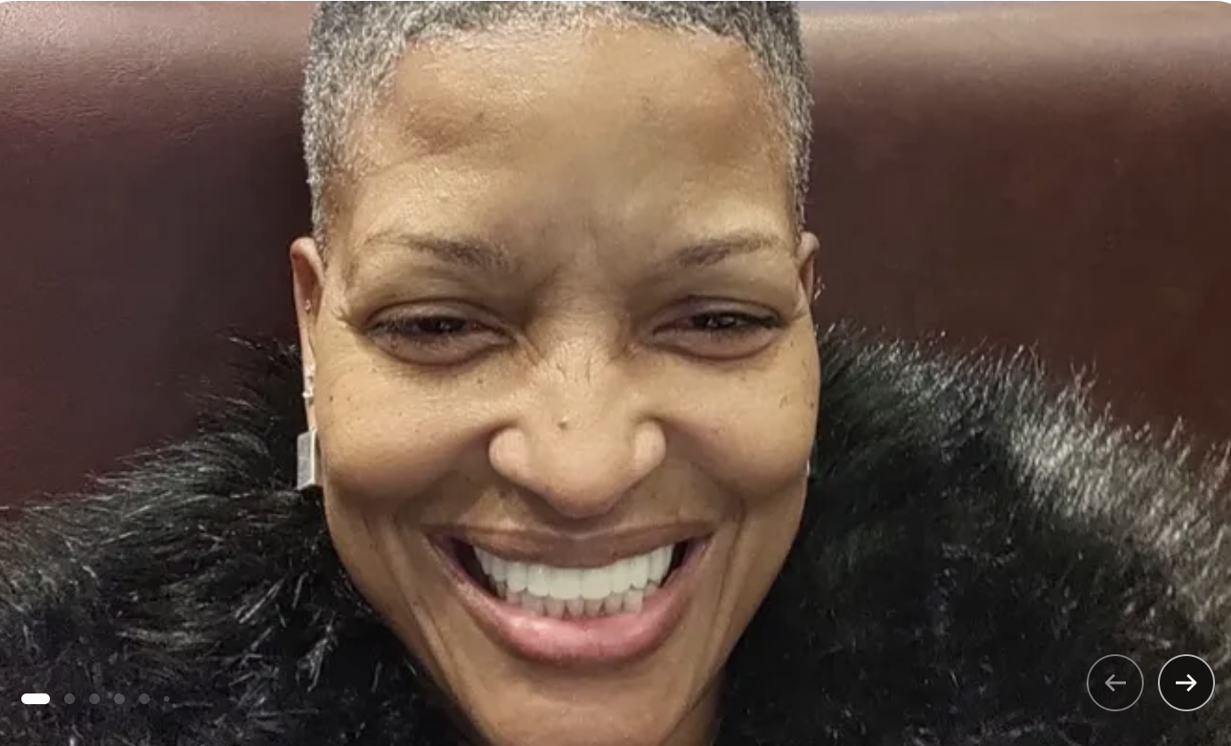 A smiling woman with short gray hair wearing a black feathered coat.