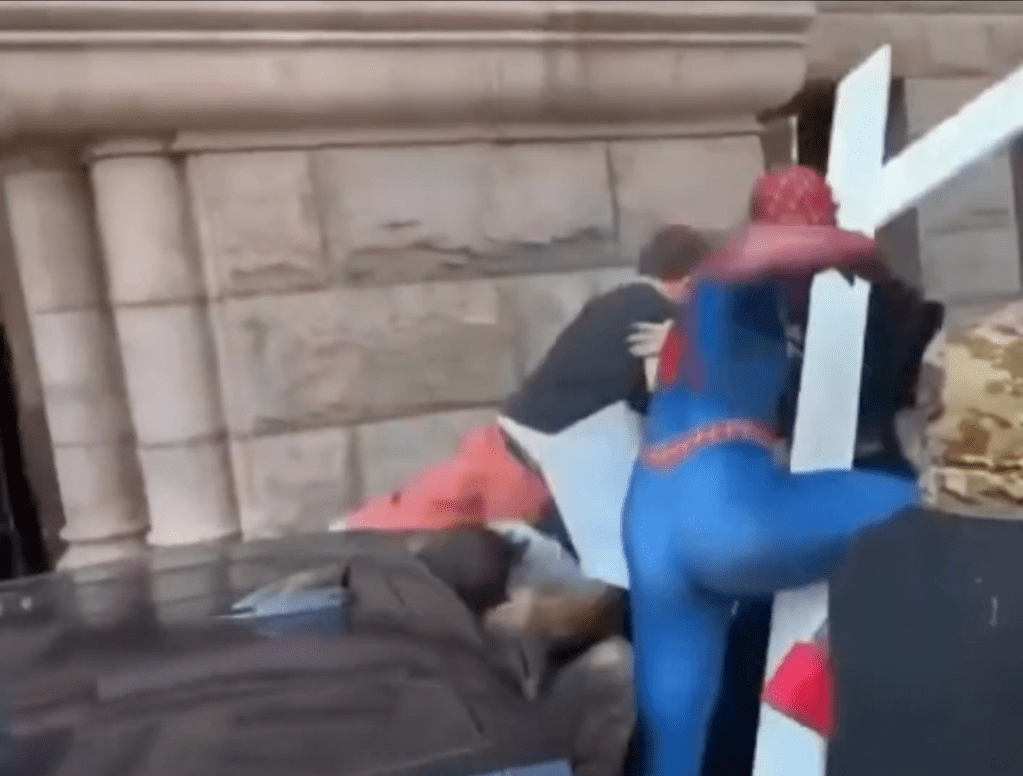 A person in a Spider-Man costume embracing another person on the ground in an indoor setting.